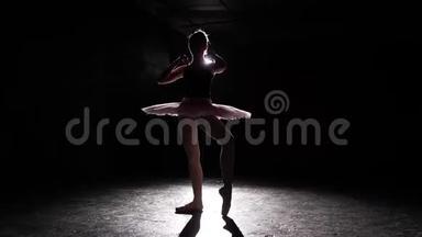 在黑色背景上分离的芭蕾舞演员剪影。 年轻的苗条芭蕾舞演员练习芭蕾。 芭蕾舞演员穿着