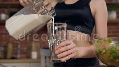 女运动员把新鲜牛奶或酸奶倒入玻璃杯中。 健康乳制品概念