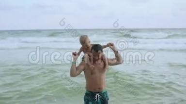 年轻的父亲和他的小儿子在海滩上玩得很开心。 儿子坐在爸爸`肩膀上