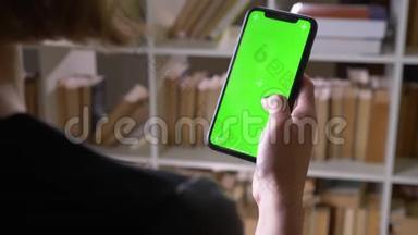 在室内图书馆用绿色彩色屏幕在手机上滚动的女学生特写后景拍摄