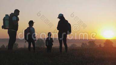 日落时父母和两个孩子在山上散步。 剪影幸福美丽的家庭
