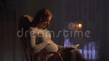 孕妇坐在黑暗<strong>的房间</strong>里<strong>的</strong>摇椅里。 女士大声朗读书给未出生<strong>的</strong>婴儿听