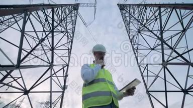男工程师正在操作平板电脑，同时站在电力线塔之间