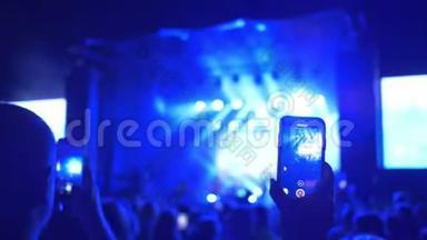 摇滚音乐会，歌迷们在手机上拍摄，在夜晚明亮的灯光下表演音乐团体
