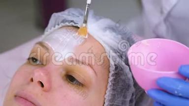 美容师用刷子把面具戴在女人`脸上。 <strong>滋润</strong>的脸。 面的特写..