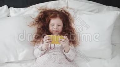 红头发的小女孩带着黄色<strong>手机</strong>躺在床上。 她笑着<strong>玩</strong>着，用智能<strong>手机</strong>慢动作。