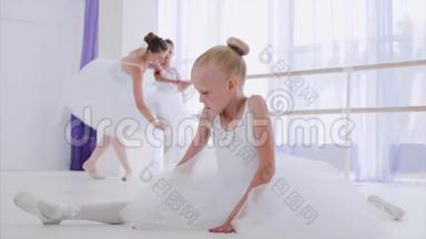 穿着白色芭蕾舞裙的小女孩芭蕾舞演员正在上芭蕾舞课做伸展运动。