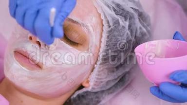 美容师用刷子把面具戴在女人`脸上。 滋润的脸。 面的特写..