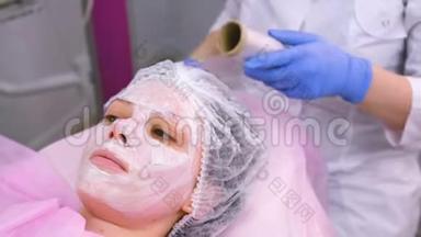 美容师把一张塑料薄膜贴在保湿面膜上面，贴在女人`脸上。