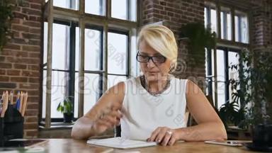 漂亮的戴眼镜的忙碌女人在办公室办公桌<strong>后面</strong>的日记里记录了一些东西。 印支。 商务