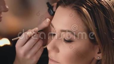 化妆师用黑色湿眼线轻轻地涂在眼睑上，用专业的刷子刷在美丽的脸上