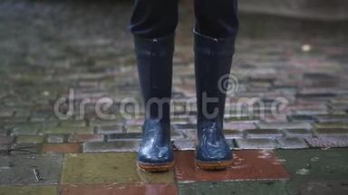 深蓝<strong>雨靴</strong>的人站在后院、城市街道或公园铺成的道路上，在大雨秋雨中。 穆迪