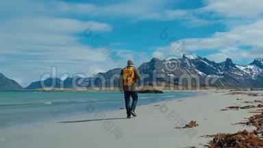 徒步旅行者穿着绿色夹克，走在遥远的沙滩上，背着一个带着大山的黄色背包，破浪前行