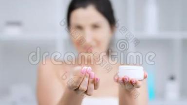 女人用罐子做白色奶油粉底，并展示奶油或面膜