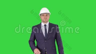 职业建筑师正在行走，拿着蓝图，这个人戴着头盔在绿色屏幕上，铬钥匙。