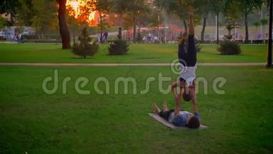 美丽的拍摄，年轻的运<strong>动男女</strong>在公园里表演一个阿克罗伊加的姿势，夕阳西下