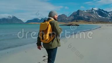 徒步旅行者穿着绿色夹克，走在遥远的沙滩上，背着一个带着大山的黄色背包，破浪<strong>前行</strong>