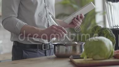 不可辨认的男人在衬衫上煮汤，检查食谱在厨房里的平板电脑上。 健康观念