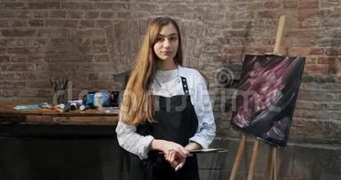 有<strong>才</strong>华的<strong>漂亮</strong>女艺术家的肖像与画笔和她的背景画布。 当代年轻女画家