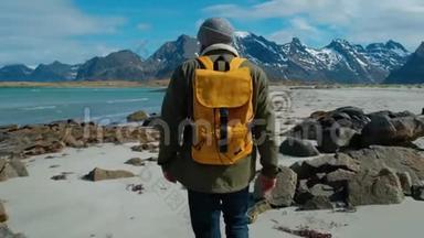 徒步旅行者穿着绿色夹克，走在遥远的沙滩上，背着一个带着大山的黄色背包，破浪<strong>前行</strong>