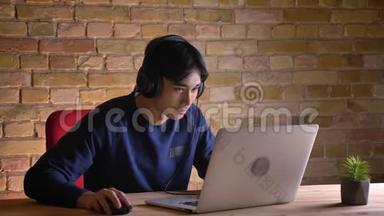 年轻有魅力的韩国男学生的特写照片，在笔记本电脑上查看，并因此而感到兴奋