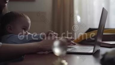 女人用手在笔记本电脑上打字，孩子阻止母亲<strong>工作</strong>。 <strong>忙碌的</strong>年轻母亲在家<strong>工作</strong>。 小儿子