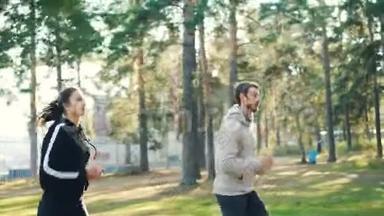 漂亮的年轻女士和她英俊的胡子<strong>男友</strong>在阳光明媚的日子在公园里慢跑。 美丽的绿树和