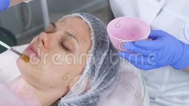 美容师用刷子把面具戴在女人`脸上。 戴着蓝色橡胶手套的美容师的手。 面部