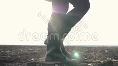 日落时分，一个农民穿着橡胶靴在阳光下的一片犁地上散步。 农业耕作
