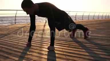 年<strong>轻</strong>的<strong>运动</strong>员在户外用他的拳头在大海或海洋前的木制泡沫上做俯卧撑。 健身和锻炼