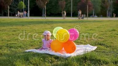 可爱的小女孩坐在城市公园的草地上，旁边放着气球，然后气球飞走了，妈妈把它们带回来