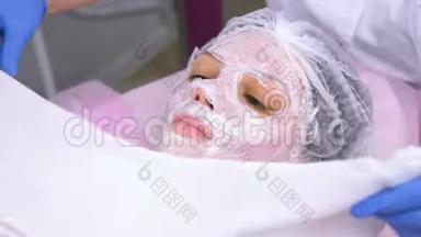 美容师用毛巾拉着女人`脸。 美容师把塑料薄膜贴在<strong>保湿面膜</strong>上