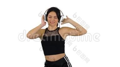 年轻快乐的运动女人听着耳机里的音乐，在白色的背景下跳舞。