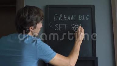 一个年轻人正在画一个`的梦想，设定目标，采取行动`在黑板上留言