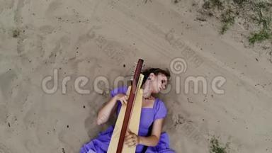 在沙漠里躺在沙滩上弹奏竖琴的女竖琴师的无人机射击。