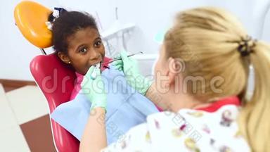 可爱的深色皮肤的非裔美国女孩坐在一个红色的黄色儿童`牙科椅上看牙医