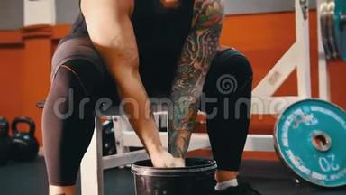 一个肌肉发达的男人用<strong>滑石</strong>粉捂着双手拍手——坐在健身房里