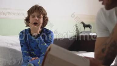 孩子坐在大床上揉眼睛，因为男孩对他哥哥为他读的书<strong>很累</strong>。 兄弟会