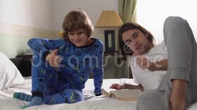 两个哥哥躺在床上，哥哥为弟弟读了一本书，他们表现得喜欢摄像。 竖起大拇指。