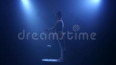 <strong>舞台</strong>上的女杂技演员站在桌子上举起但向上。 烟雾<strong>蓝色</strong>背景。 慢动作