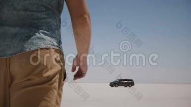 特写镜头跟随着穿着休闲服装的年轻放松男子，在犹他州盐湖沙漠中心朝汽车走去。