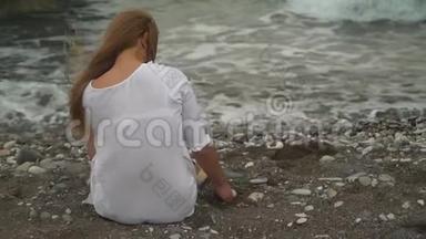 年轻女子坐在海滩上，在海边玩沙子