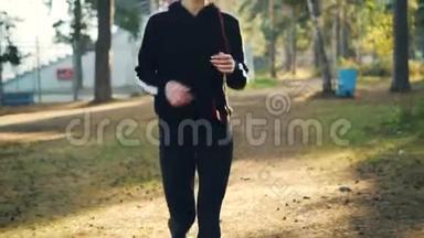 穿着运动鞋和运动服的漂亮年轻女士戴着耳机在公园慢跑，享受身体健康