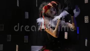 穿着一件连衣裙，戴着一顶戴着小铃铛的红帽子的可怕的小丑女孩正在做鬼脸，摇头