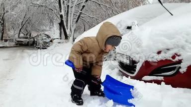 雪灾后，小男孩在雪地里锯车的4K镜头。 孩子用铲子挖雪