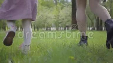 年轻的妈妈和<strong>小女孩</strong>的腿在公园里<strong>奔跑</strong>，在绿草上紧紧地牵着手。 积极健康