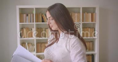 一位年轻漂亮的白种人女学生在图书馆里看书和看照相机的特写镜头
