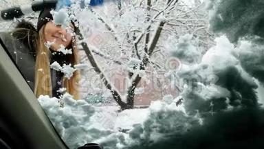 来自汽车司机座<strong>位</strong>的4k视频，年轻微笑的女人在暴风雪后清理汽车<strong>挡</strong>风玻璃