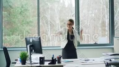 这位玩得很开心的年轻女士正在办公室里跳舞，她一边<strong>甩头</strong>发，一边摘下眼镜，一边笑，一边走