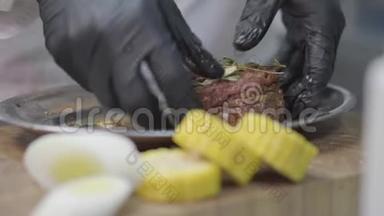 厨师双手戴着blsck手套，在金属盘子里摩擦一块小牛肉，腌制肉。 靠近盘子的甜玉米。 慢动作